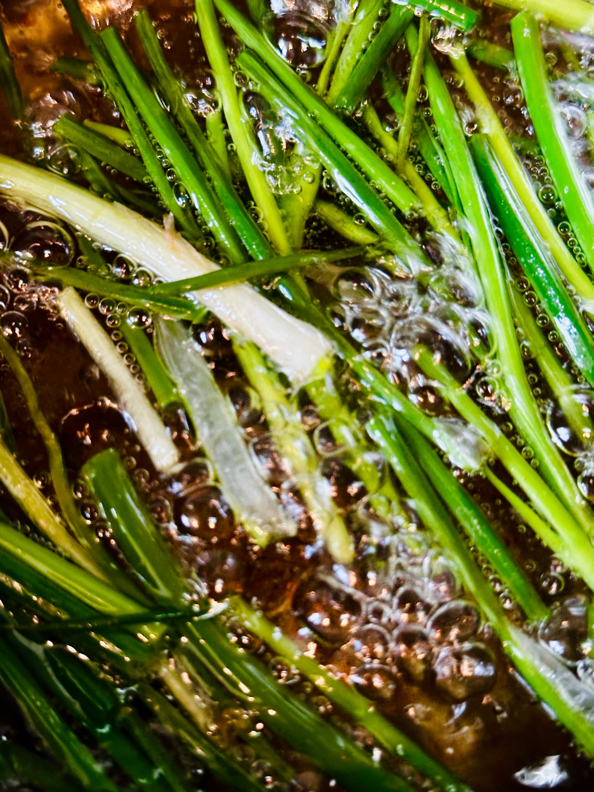 Green stocks from scallions in a golden brown oil, bubbling.