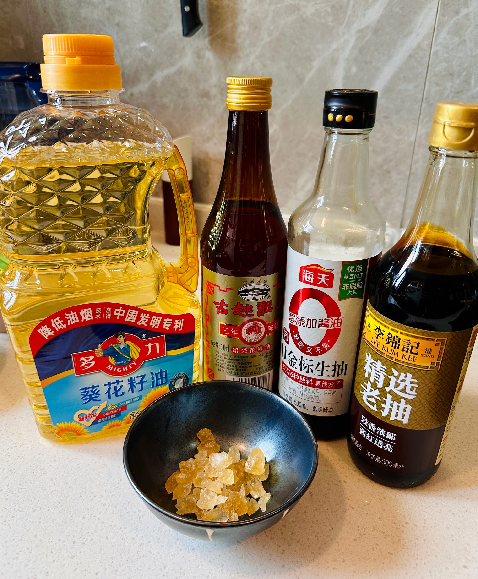 Various soy sauces and oils with yellow rock sugar on a counter.