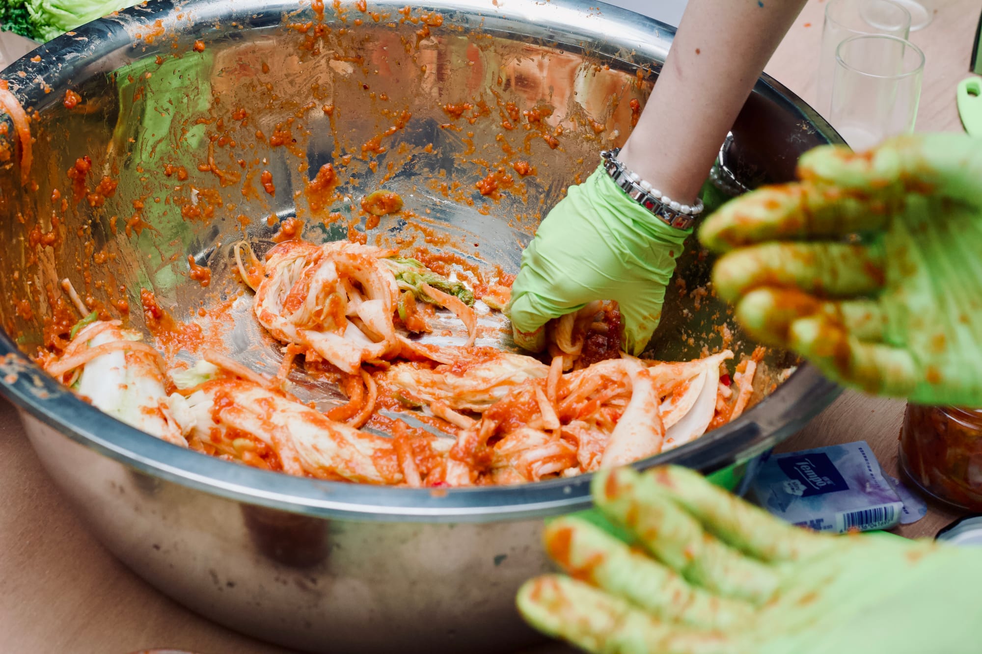 A large stainless steal bowl with the initial ingredients for kimchi, being mixed by hand