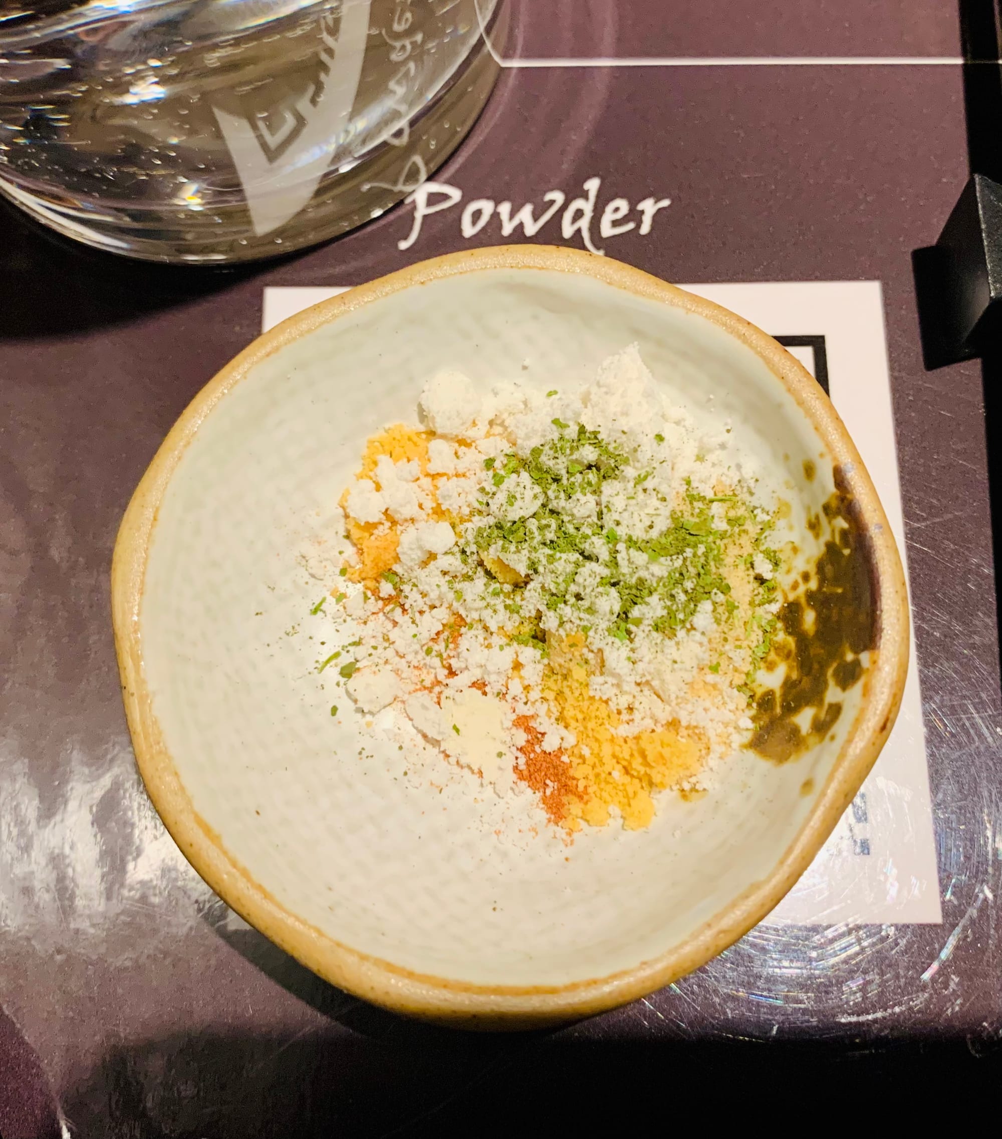 A white dishes with yellow, green, white, and orange powders.