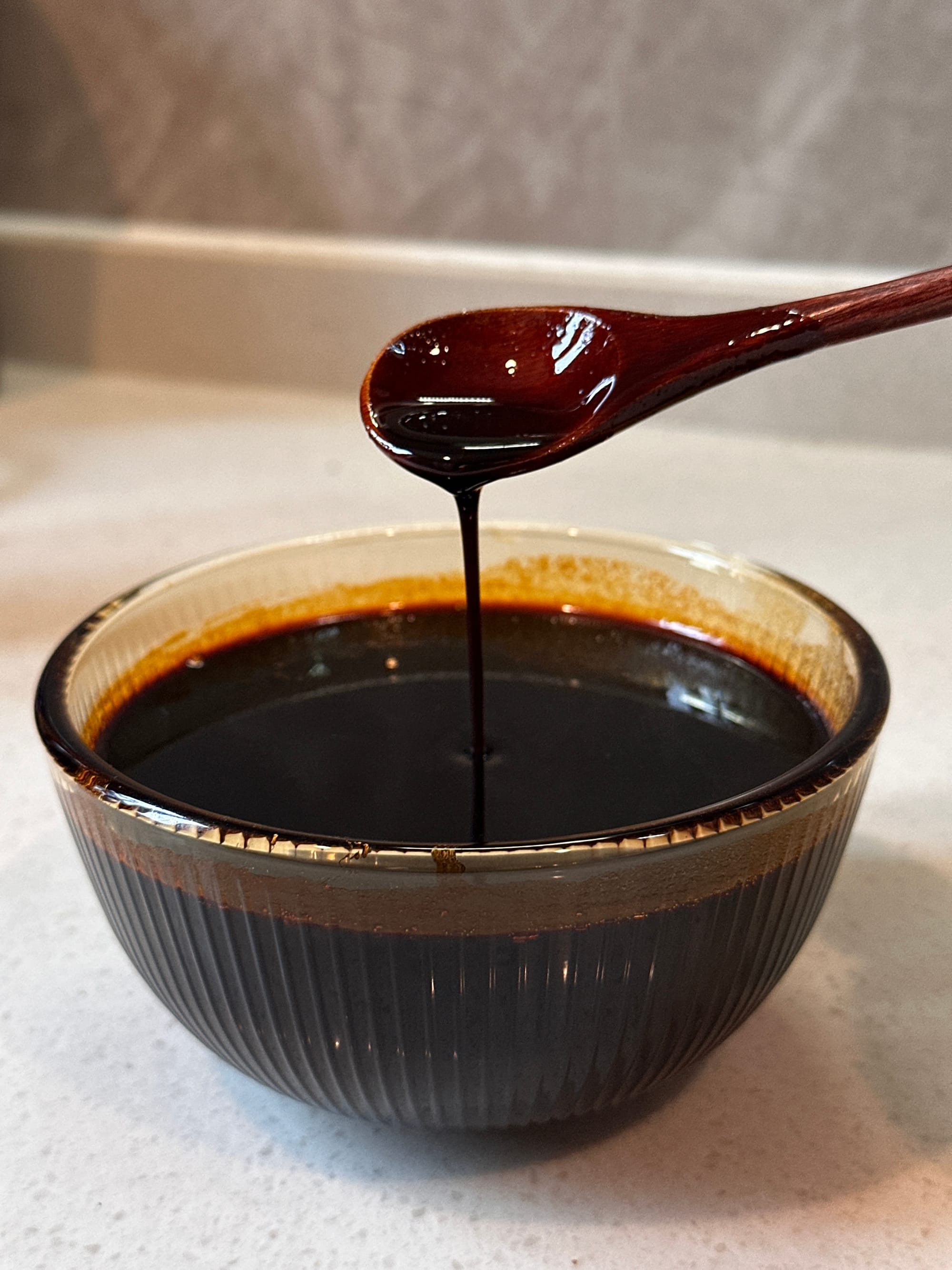 Compound soy sauce being dripped into a clear bowl from a wooden spoon.