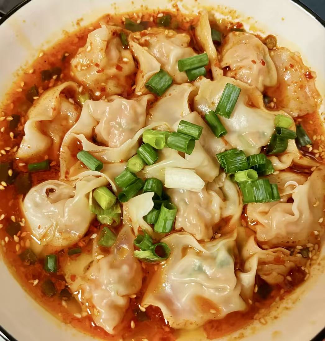 Wontons covered in red chili oil and green onion