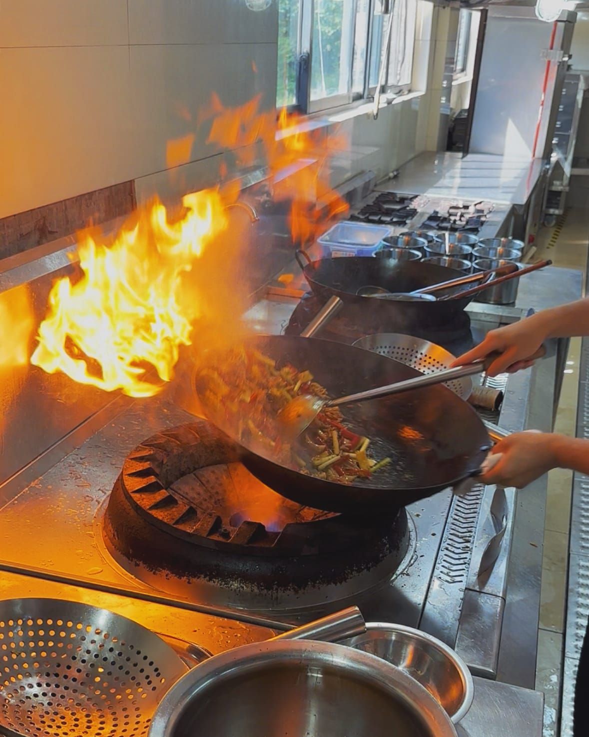 Professional chef stir-frying using a wok and professional gas stove in a professional kitchen with fire shooting out.