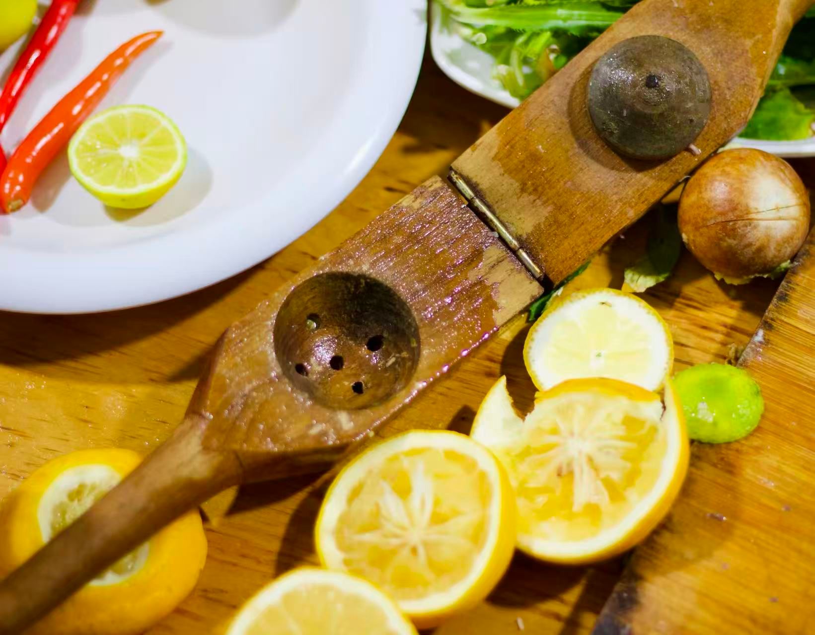 A wooden hand-juice press for lemons, limes, etc. sits on a wooden table next to pressed lemons.