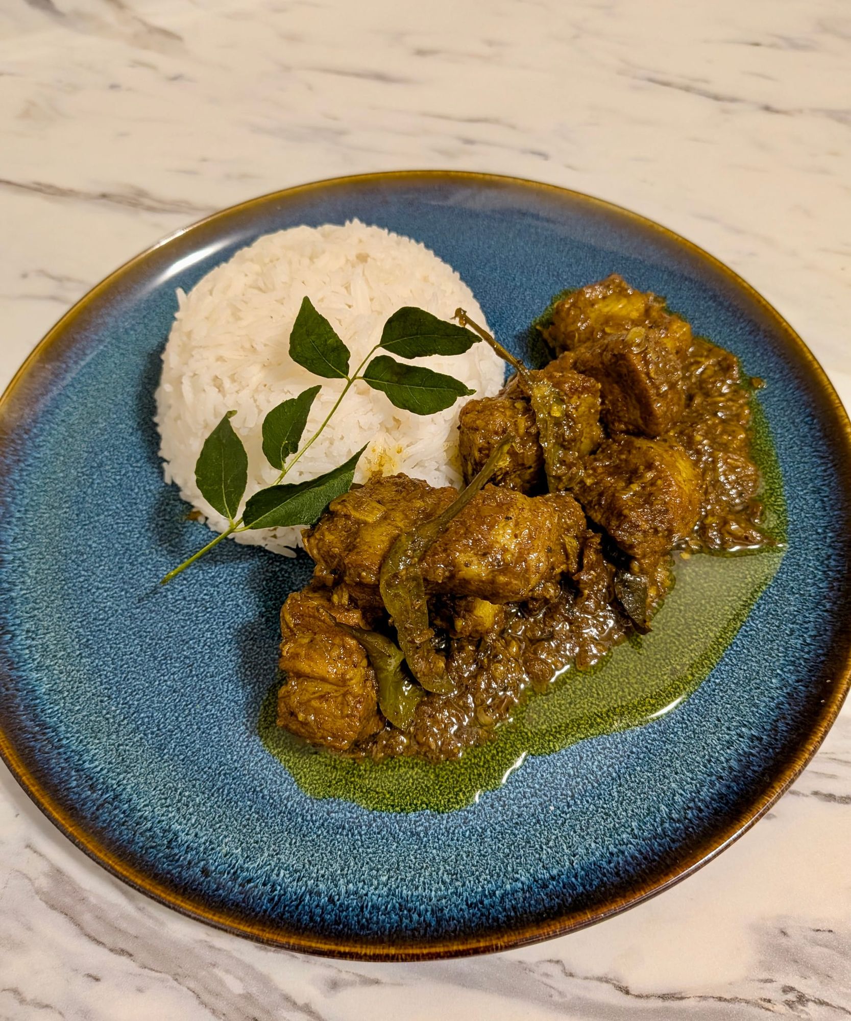 Sri Lankan Black Pork Curry on a blue plate with white rice.