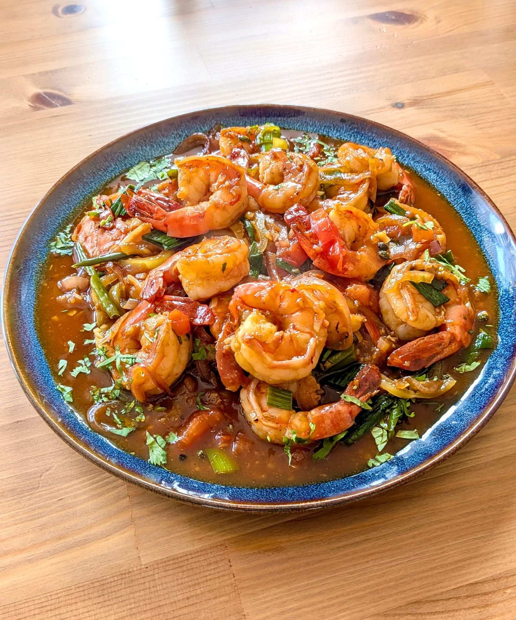 Mala Devilled Prawns in a bowl - golden red prawns covered in a brown sauce with green garnish.