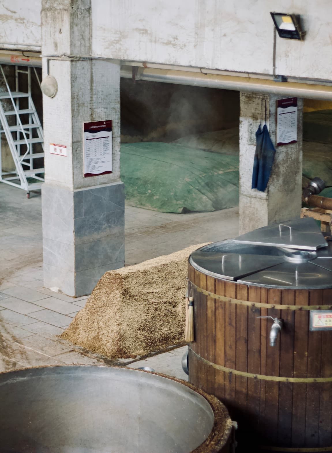 A look inside an industrial warehouse where baijiu is using mud pits to ferment, steam rises during the fermentation process.