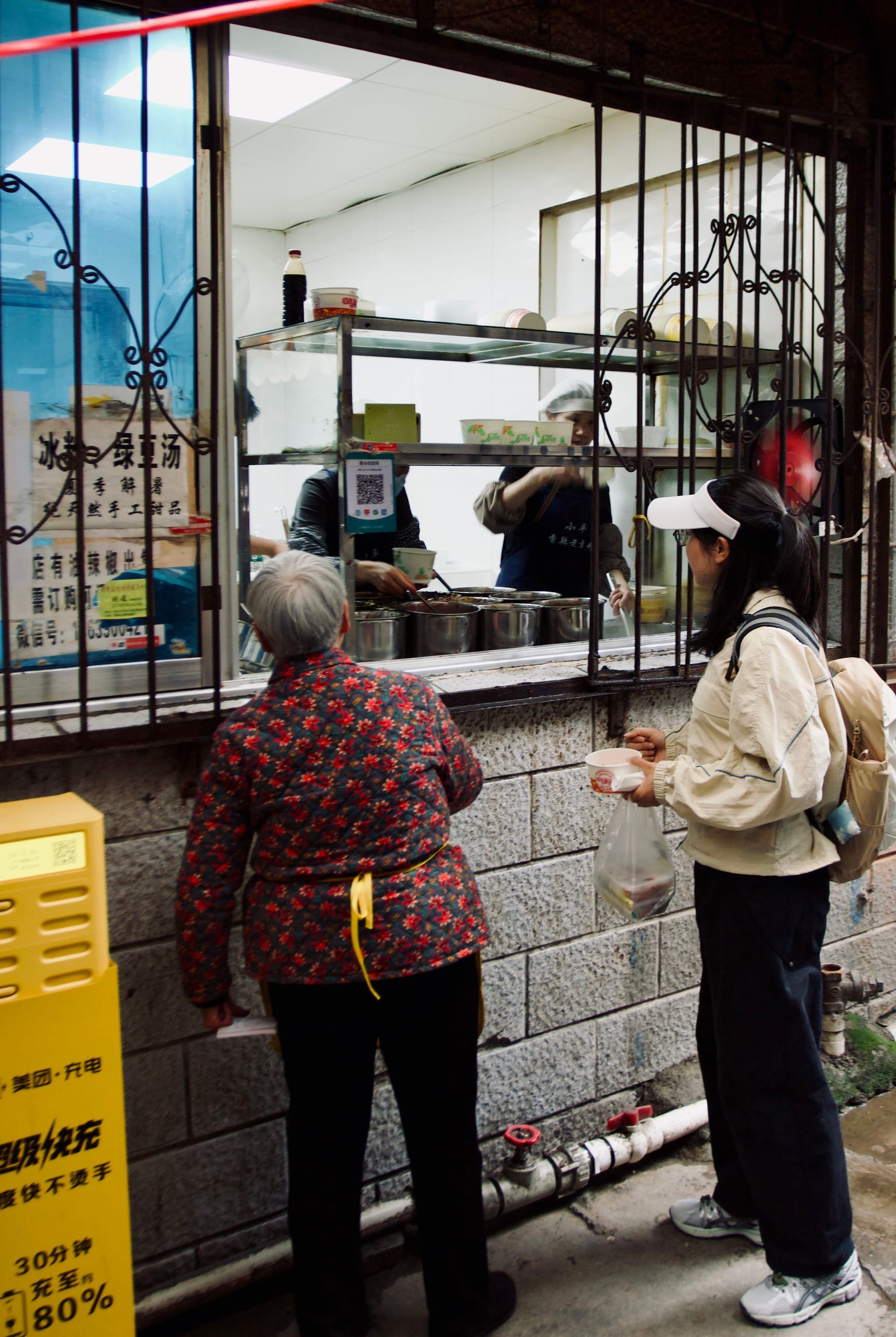 A restaurant serving window sits in a residential building, with customers lined up outside.