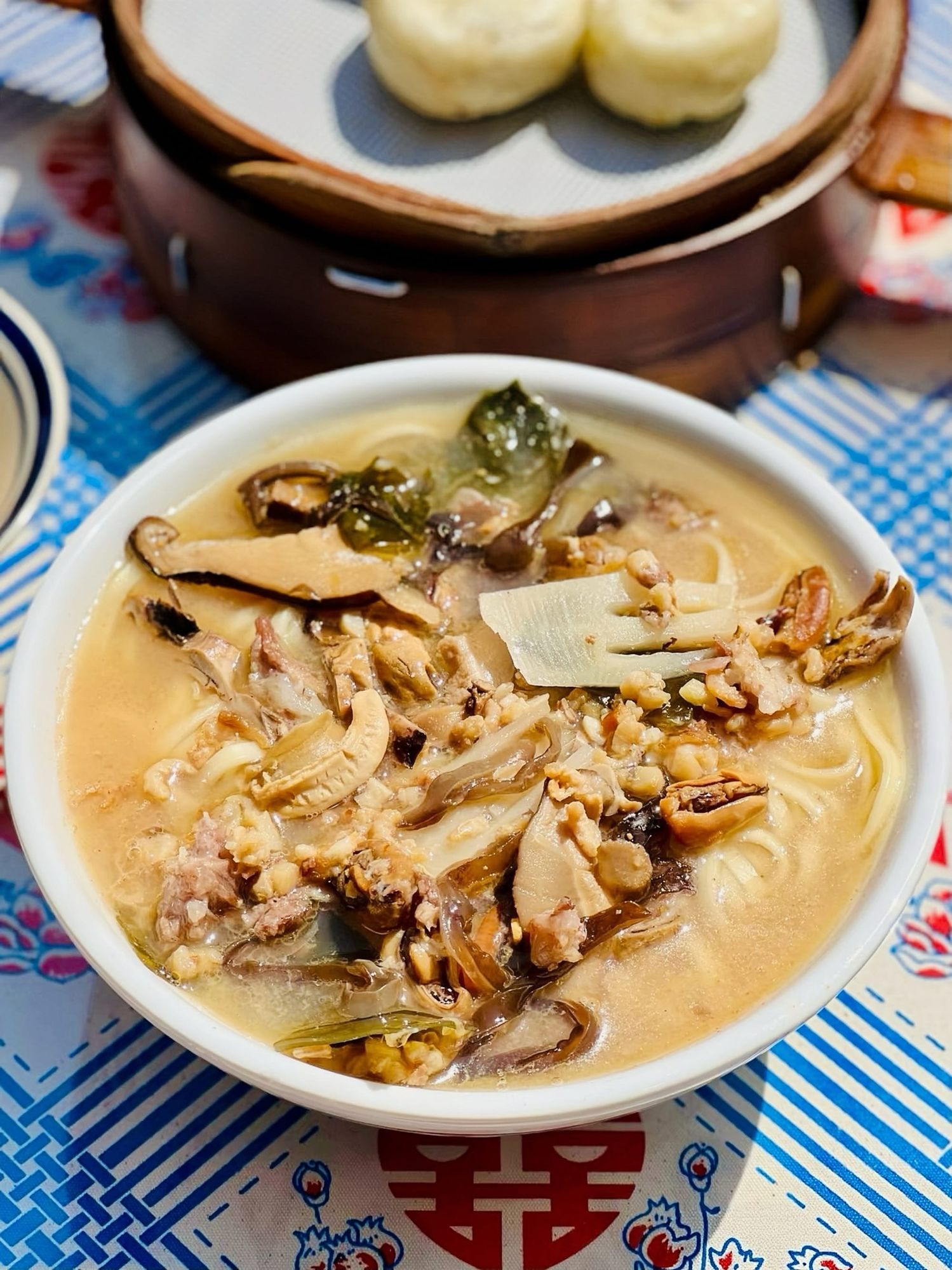 A bowl of beige haiwei noodles featuring mushrooms and chicken in a white bowl.