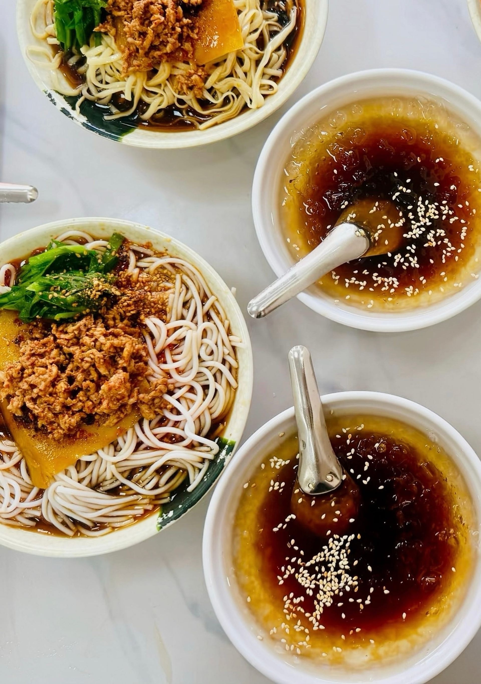 A bowl of noodles, topped with minced pork sits next to two bowls of se shui sauce - a clear, glass-like looking sweet cold sauce.