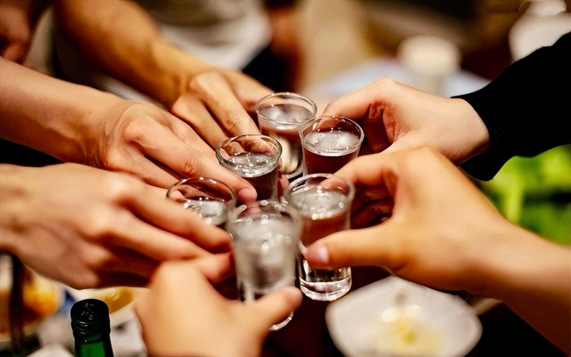 Six hands holding out baijiu shot glasses clinking them together as a group.