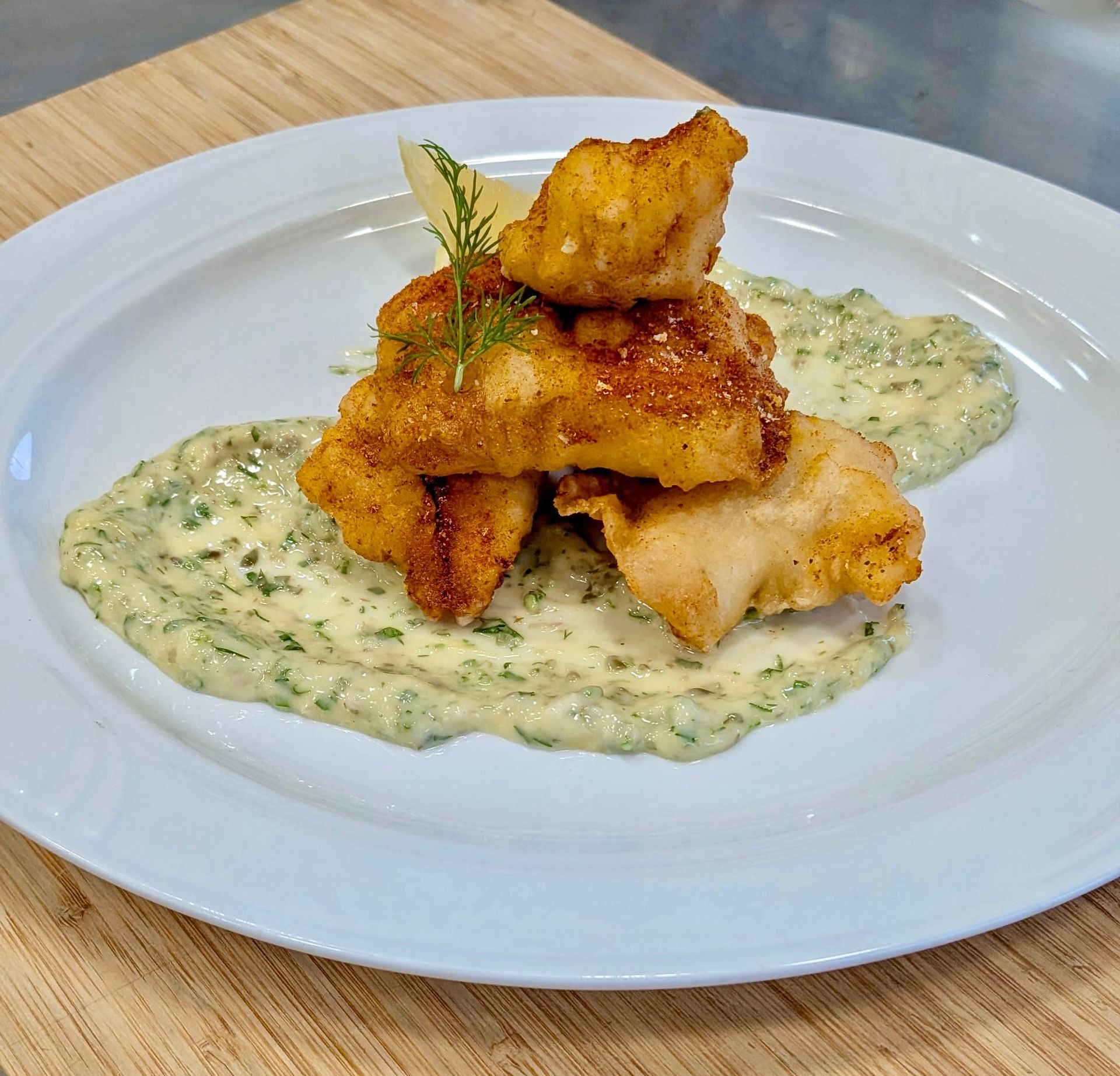 Crispy golden fried kibbefish pieces stacked neatly on top of each other and a ravigotte sauce on a white plate