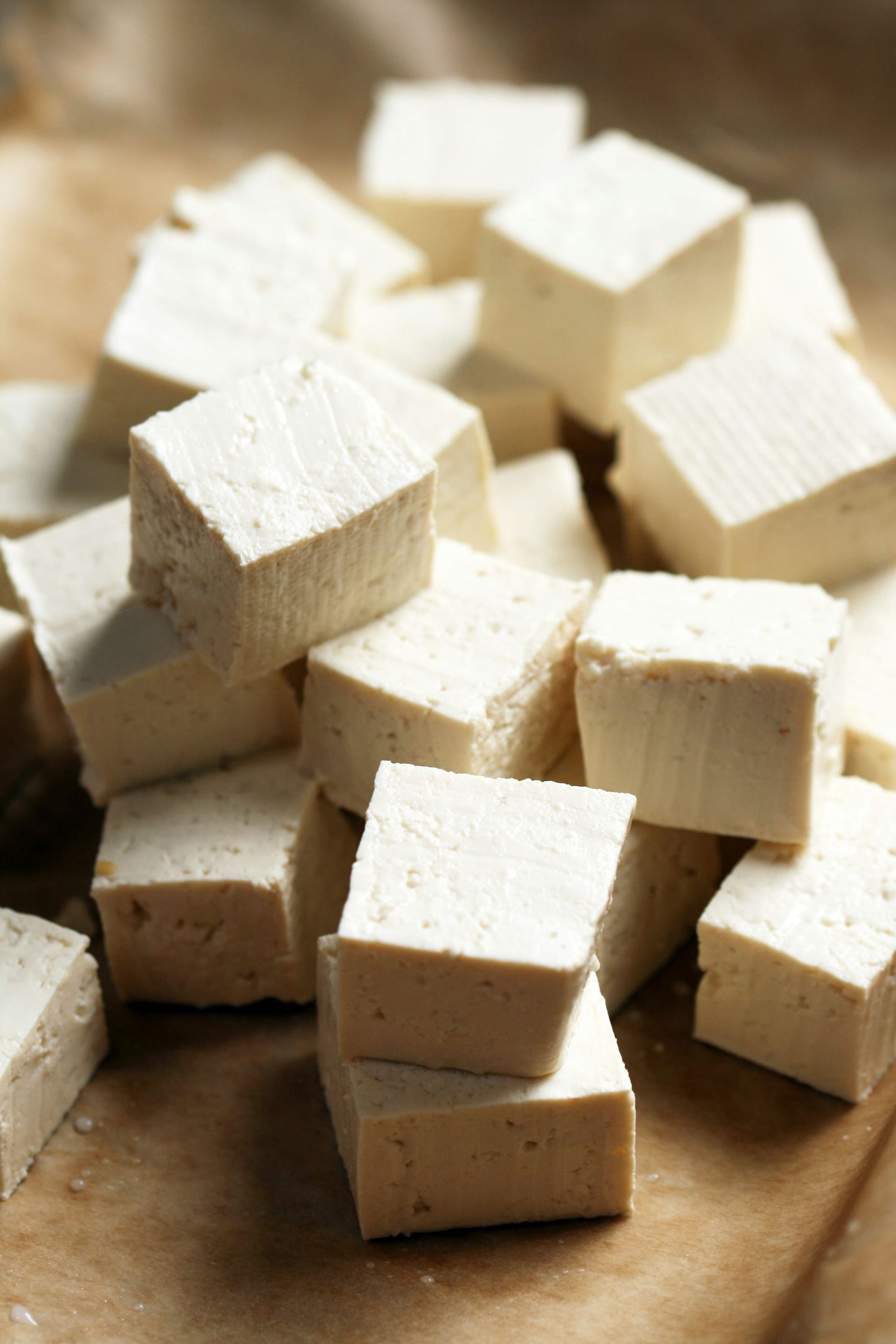 A small loose pyramid stack of white tofu cubes on a cutting board.