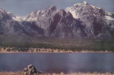A scan of an old painting of rocky mountains in Yunnan before a forest and river in the foreground.