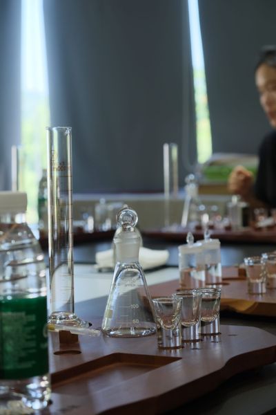A baijiu mixing kit setup: large beakers, a bottle of water, tasting cups, and a pen sit upon a wooden tray.