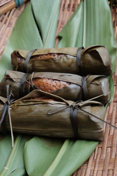 Two Huangba wrapped in their leaves, spilling out onto a pair of leaves and bamboo.