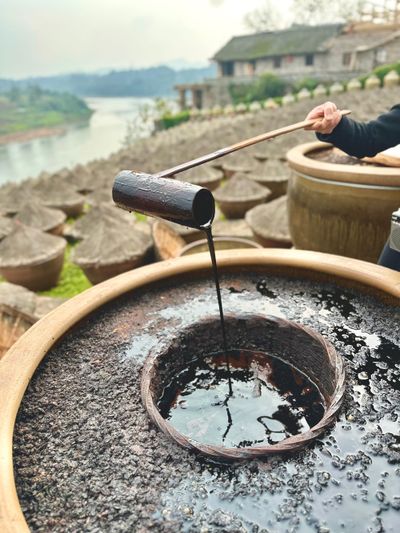 A bamboo ladle pours dark rich soy sauce back into the centre of a soy sauce fermentation urn from whence it came. 