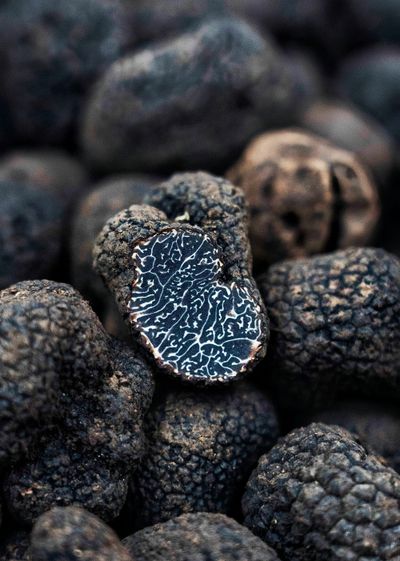 A closeup photo of black truffles. In the center of the pile, one is sliced in half, showing a wavy black and white pattern inside.