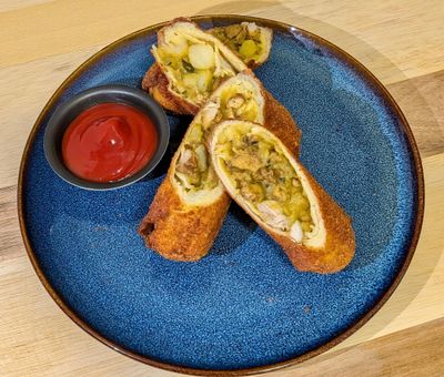 Plated chicken rolls sliced in half, leaning on each other with a dipping saucer of ketchup.