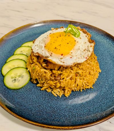 Nasi Goreng fried rice with diced cucumbers on the side and a fried egg on top, on a blue plate.