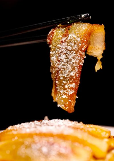 Chopsticks holding a piece of Jia Sha Rou - a piece of pork covered in granulated sugar.