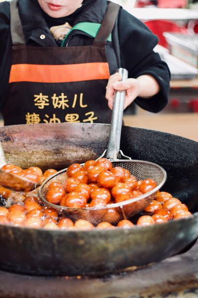 Round golden-red dough balls soaked in oil sit in a sieve as they fry in a large fire-heated wok.