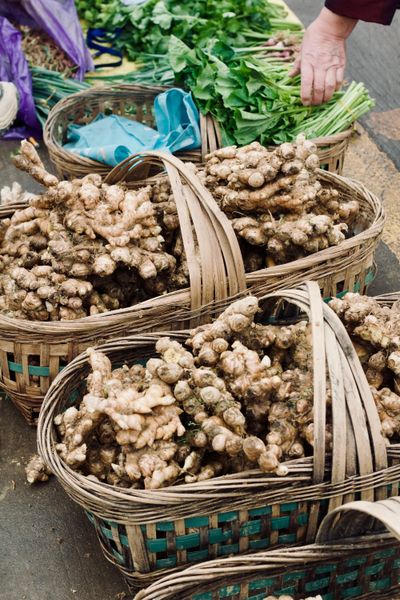 Large bamboo baskets filled with giant spring ginger sit on a market floor, ready to be purchased.