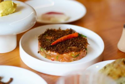 A white plate with a circular salmon tartare base topped with fermented brown ants and a pickled chili pepper