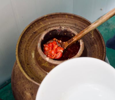 A spoon taking out fermenting tomatoes from a brown ceramic urn.
