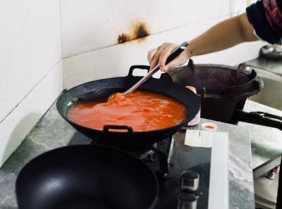 Two black cooking woks sit on a stove, one empty, and the other filled near to the brim with red sour soup.