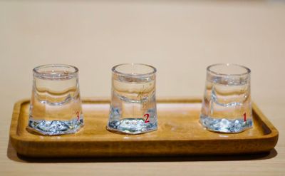 Three clear shot glasses with wide thick bottoms that taper to a narrower top sit on a wood serving tray, each filled with different aged baijiu