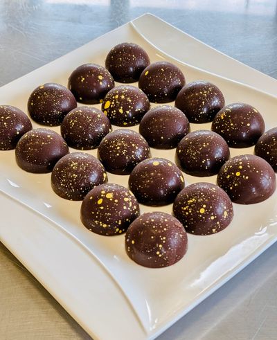 A white tray with 20 brown chocolate bonbon domes specked with yellow dots.