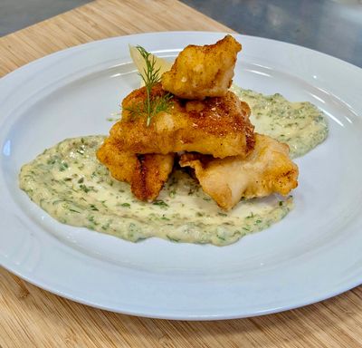 Crispy golden fried kibbefish pieces stacked neatly on top of each other and a ravigotte sauce on a white plate