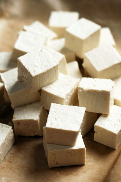 A small loose pyramid stack of white tofu cubes on a cutting board.
