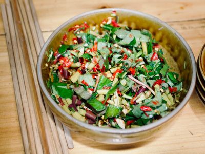 A clay bowl with a mixed assortment of green and red - chopped vegetables.