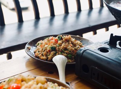 A wooden table with a portable stove next to a plate of fried rice made with fermented vegetables 