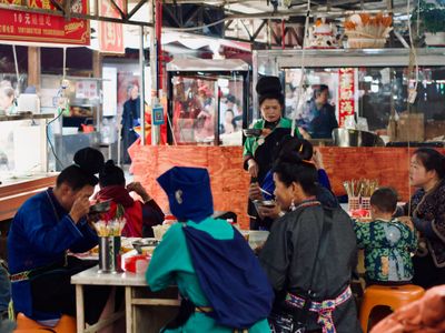 A morning market eatery is packed with local Miao people eating from bowls.