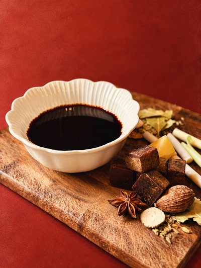 Compound soy sauce in a white dish on a wooden cutting board surrounded by its raw ingredients.