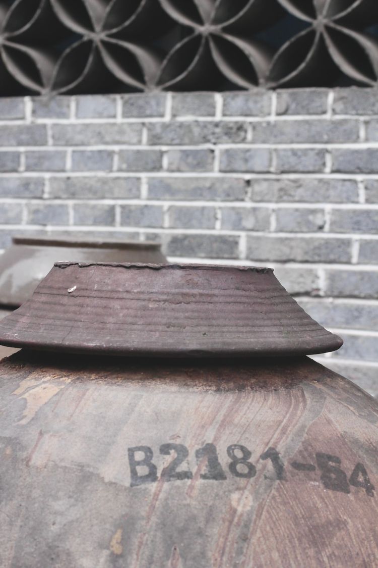 The top of a brown weather-worn ceramic vinegar jar stamped with its vat number in black ink.
