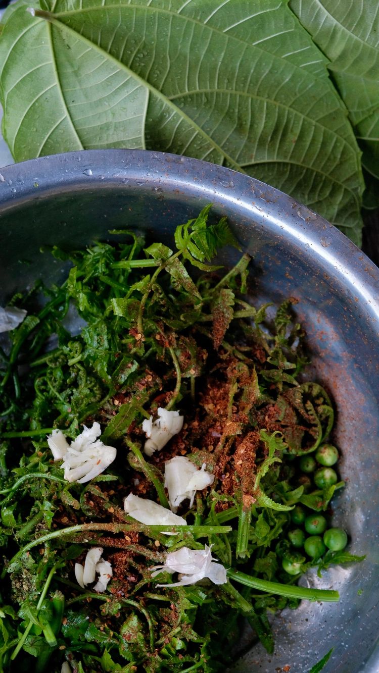 Local wild greens, green peas, garlic, and chili pepper powder tossed together in a mixing bowl.