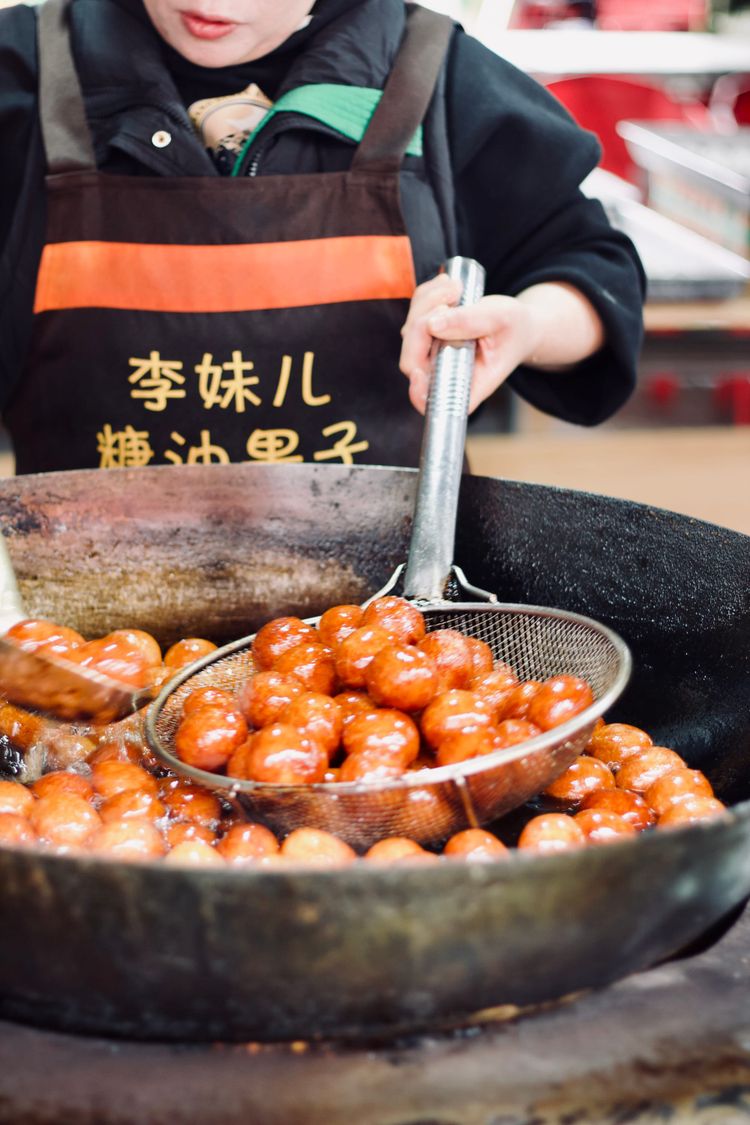 Round golden-red dough balls soaked in oil sit in a sieve as they fry in a large fire-heated wok.