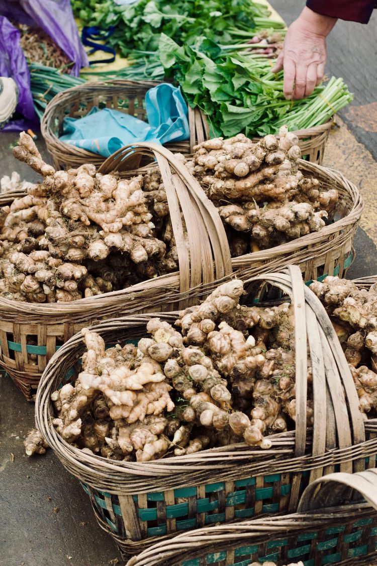 Large bamboo baskets filled with giant spring ginger sit on a market floor, ready to be purchased.