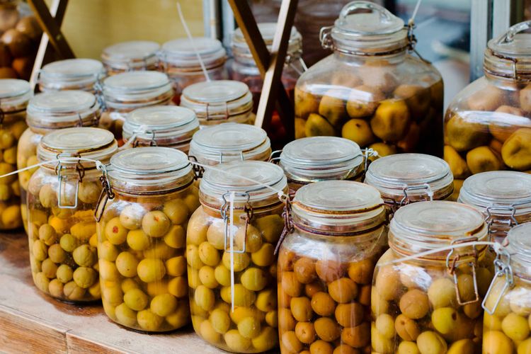 Many mason jars filled with fermenting green plums to be used for drinks or seasoning.