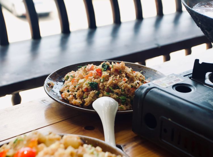 A wooden table with a portable stove next to a plate of fried rice made with fermented vegetables 