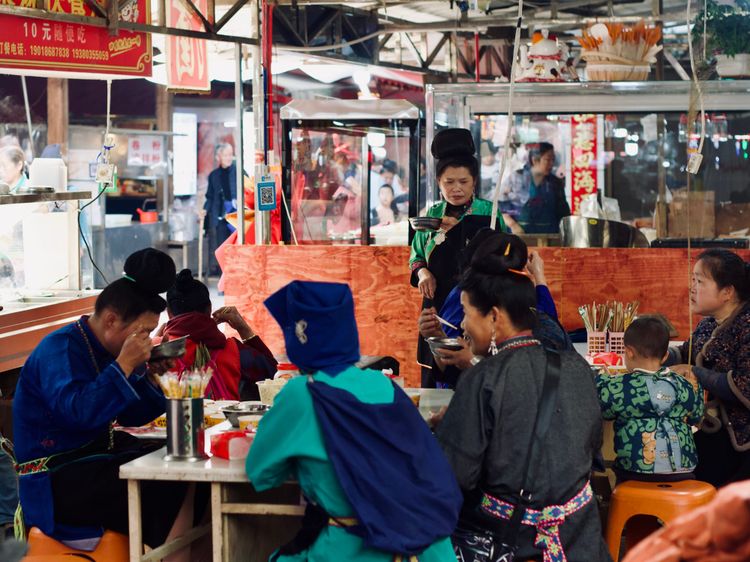 A morning market eatery is packed with local Miao people eating from bowls.