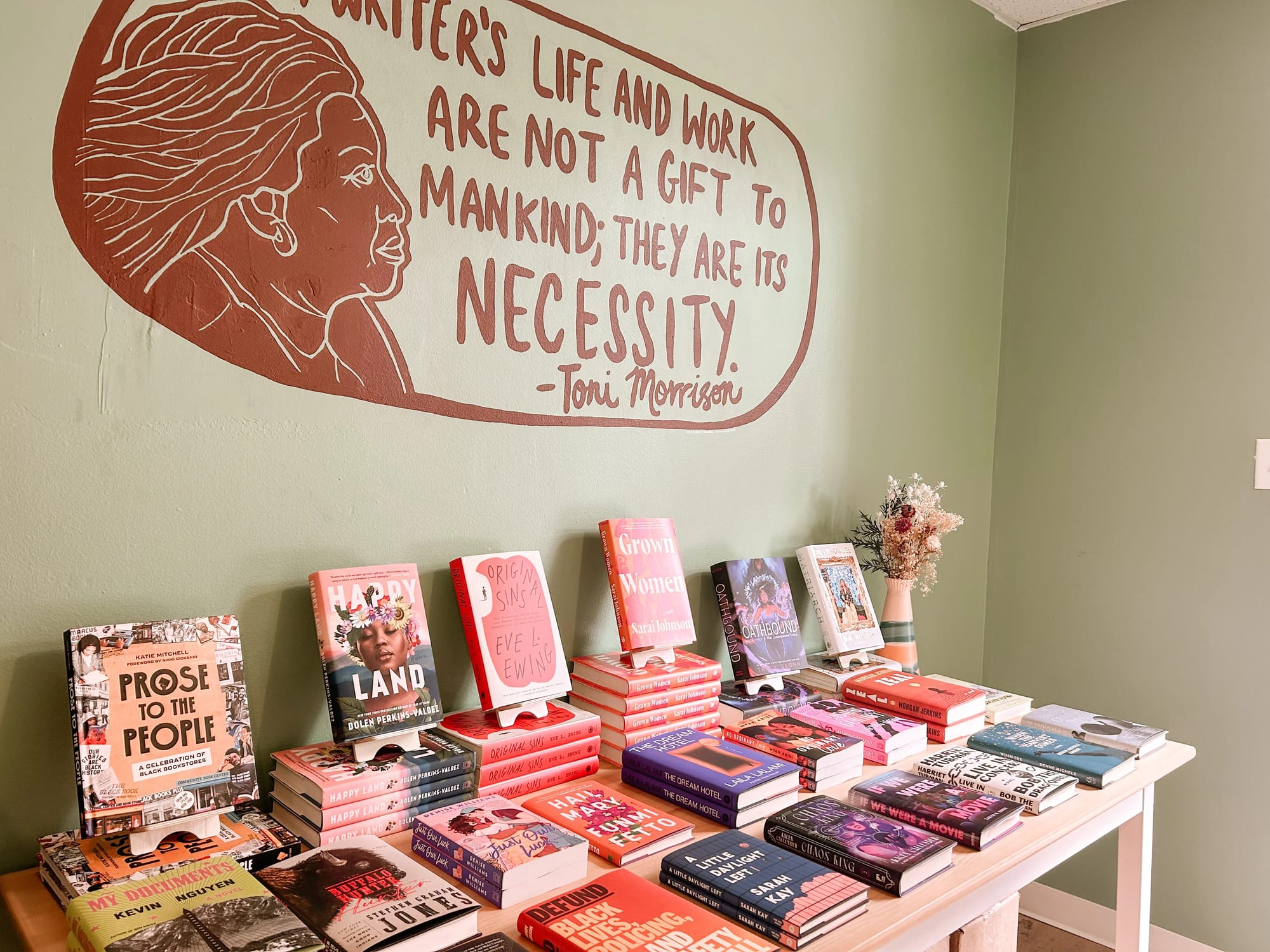 Angled view of a neatly arranged display table with a mostly visible Toni Morrison quote painted on the wall above: "A writer's life and work are not a gift to mankind; they are its necessity."