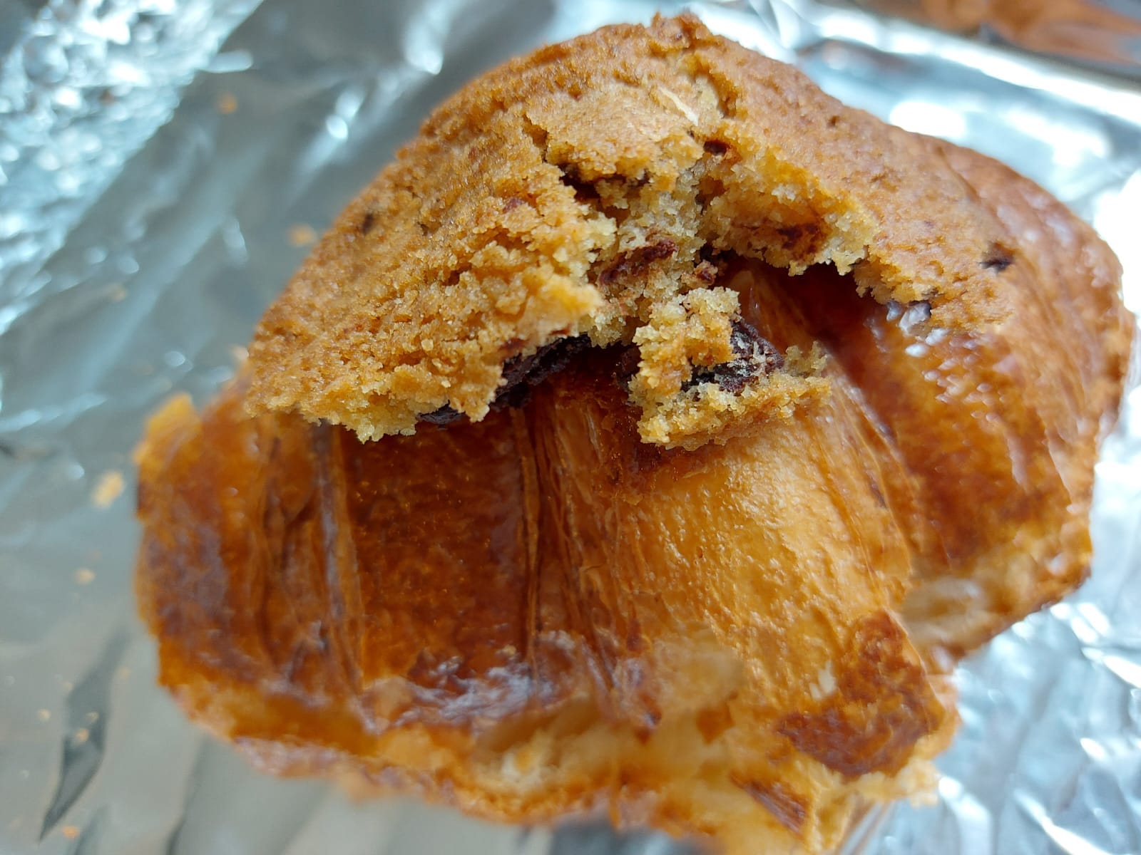 Croissant on aluminum foil with a small portion of cookie on top, molded to the shape of the croissant