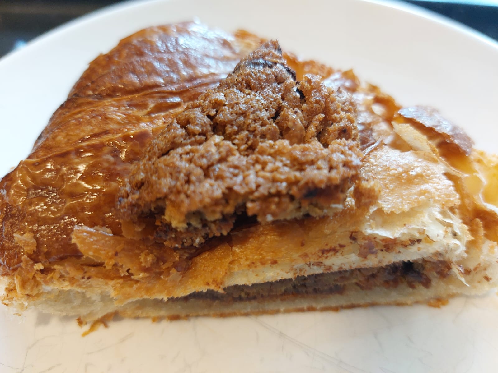 Angled side view of cut croissant on white plate with cookie garnish on top, showing that the whole thing looks like an actual dessert someone might serve you on a plate
