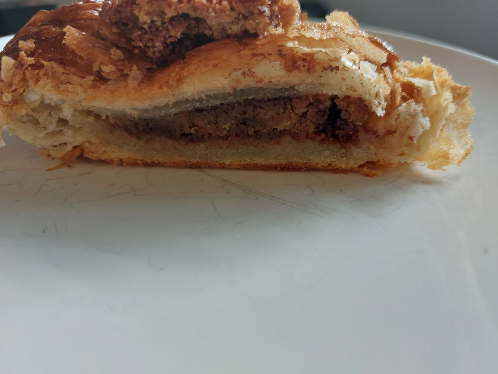View of cut croissant on white plate from side, showing the moist, crummy cookie filling up close, with the flaky croissant surrounding it like a crust