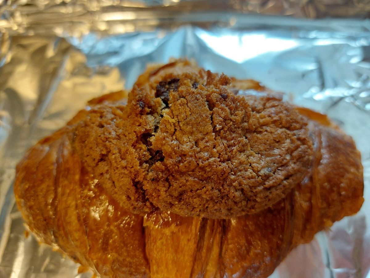 Photo of a croissant topped with a portion of chocolate chip cookie, resting on a sheet of aluminum foil